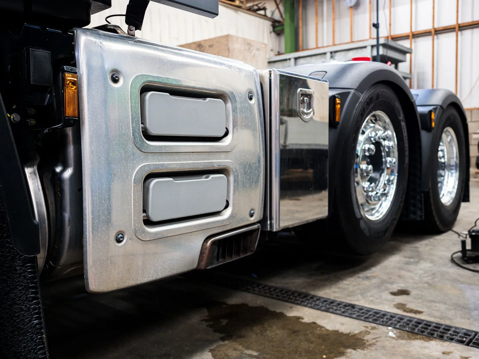 Detail of a tractor unit's polished side fairing and drive wheels in a workshop